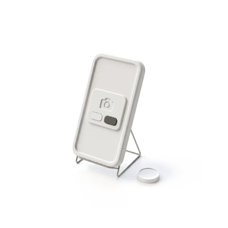 A ceramic phone showing a camera-access dialog with two buttons, one in graphite, a lens cap beside it.