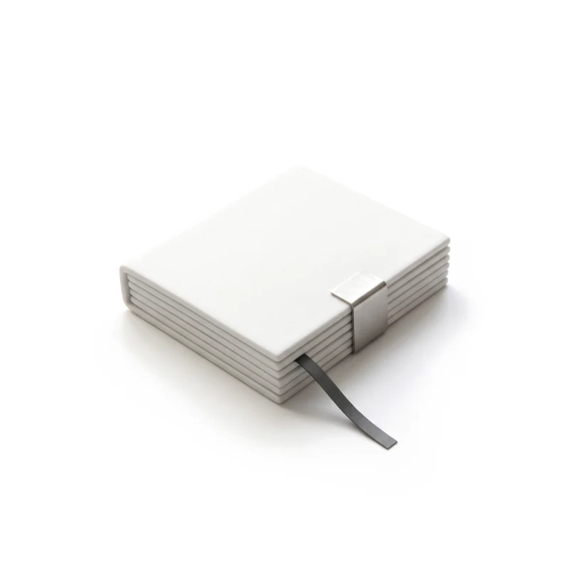 A closed ceramic folder on a short stack of ceramic sheets, held by a steel clip, a graphite ribbon marking a page.
