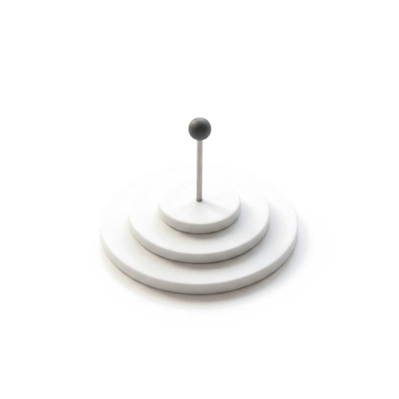 Stacked white ceramic discs forming a shallow target, a thin steel pin with a graphite head in its centre.