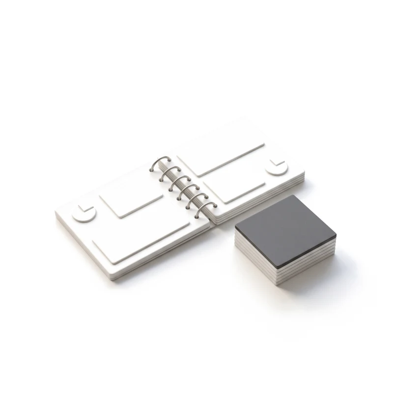 An open white ceramic booklet on steel rings, beside a stack of ceramic cards topped with graphite.