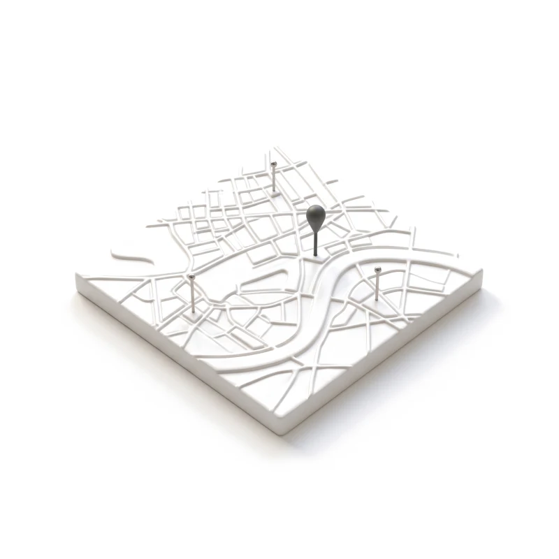 A white ceramic city-map tile with raised streets and a river, three steel pins and one graphite pin.