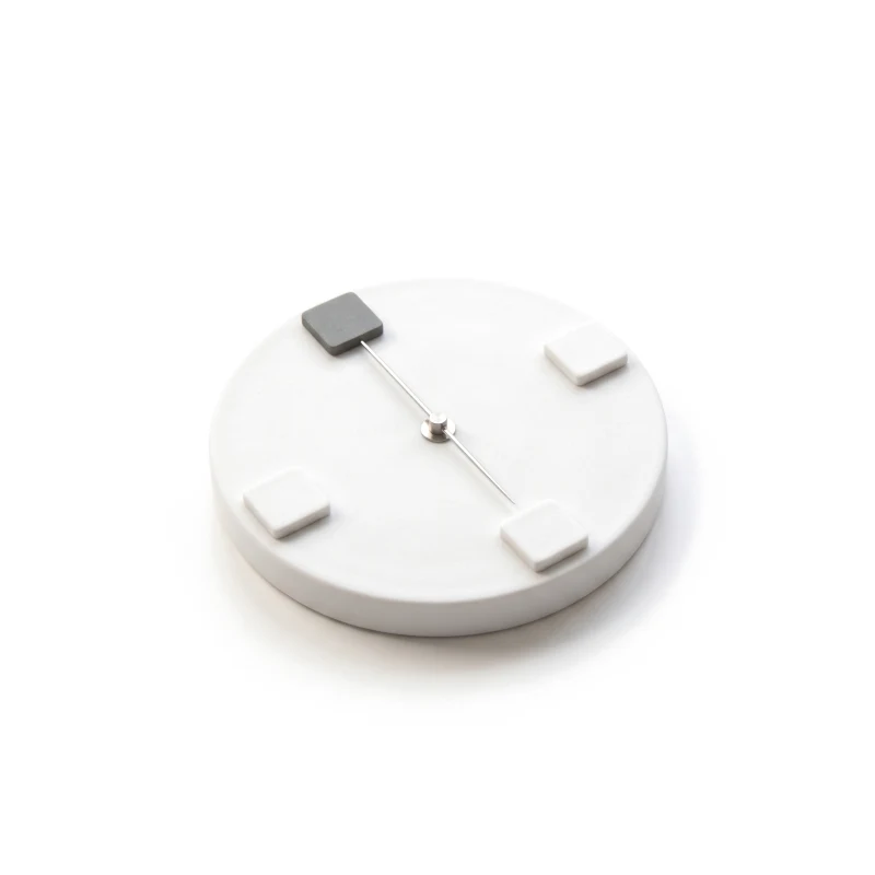 A round ceramic compass base with a thin steel needle pointing at one of four small tiles, that tile graphite.