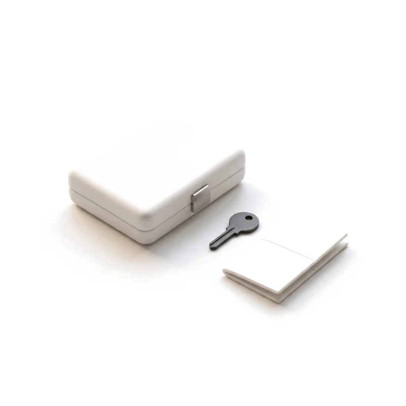 A closed white ceramic case with a steel latch, a graphite key and a small booklet beside it.