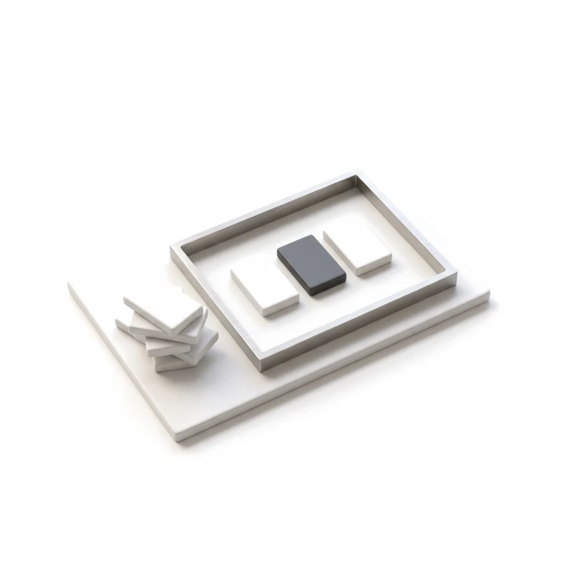 A steel frame on a white ceramic plate holding three blocks, one graphite, with other blocks stacked aside outside it.