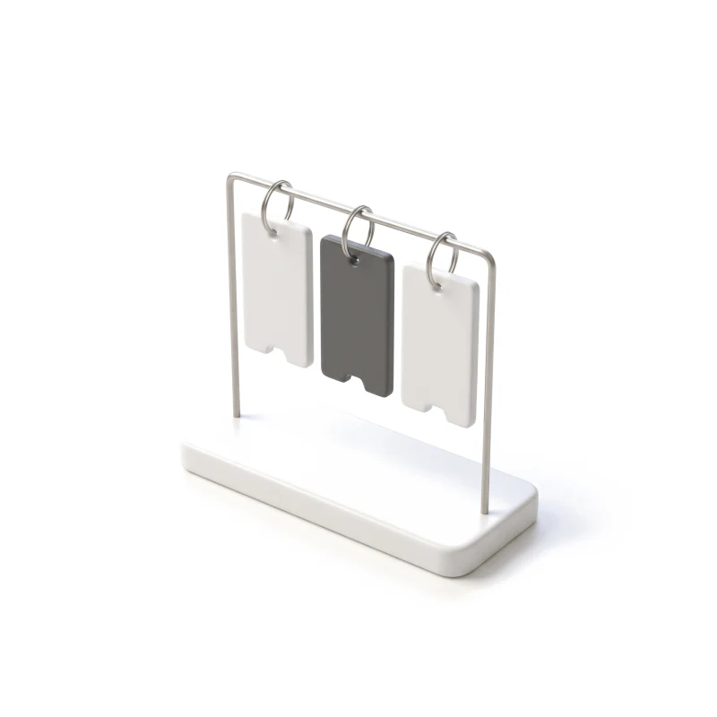 Three ceramic staff badges on steel rings hanging from a rail on a ceramic stand, the middle one graphite.