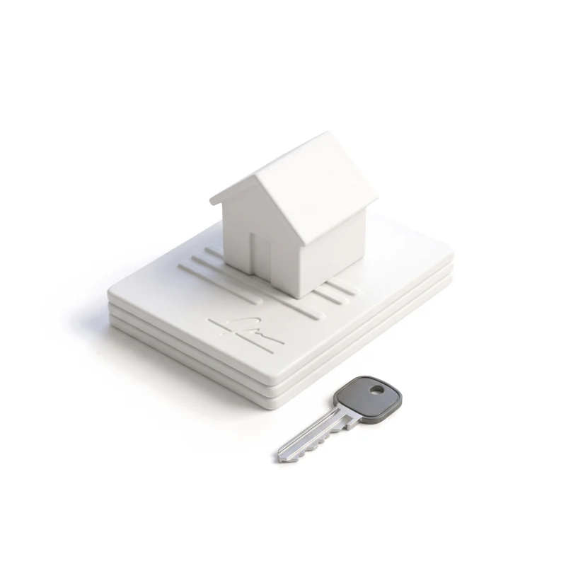 A small ceramic house on a stack of ceramic sheets, a steel key with a graphite head in front.