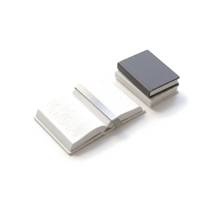 An open white ceramic book with a steel bookmark strip, two closed ceramic books beside it, the top one graphite.