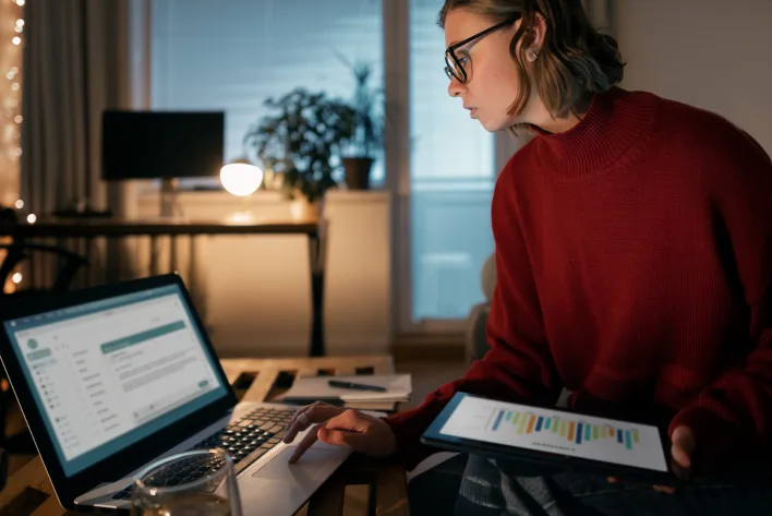 A woman in a red sweater works on a laptop and tablet, focusing on dashboard design and functionality.