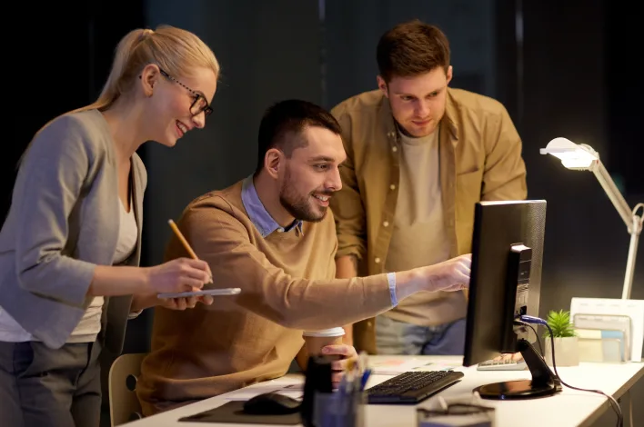 Three professionals collaborating on a computer in an office, showcasing ANODA UX Design Agency’s award-winning projects.